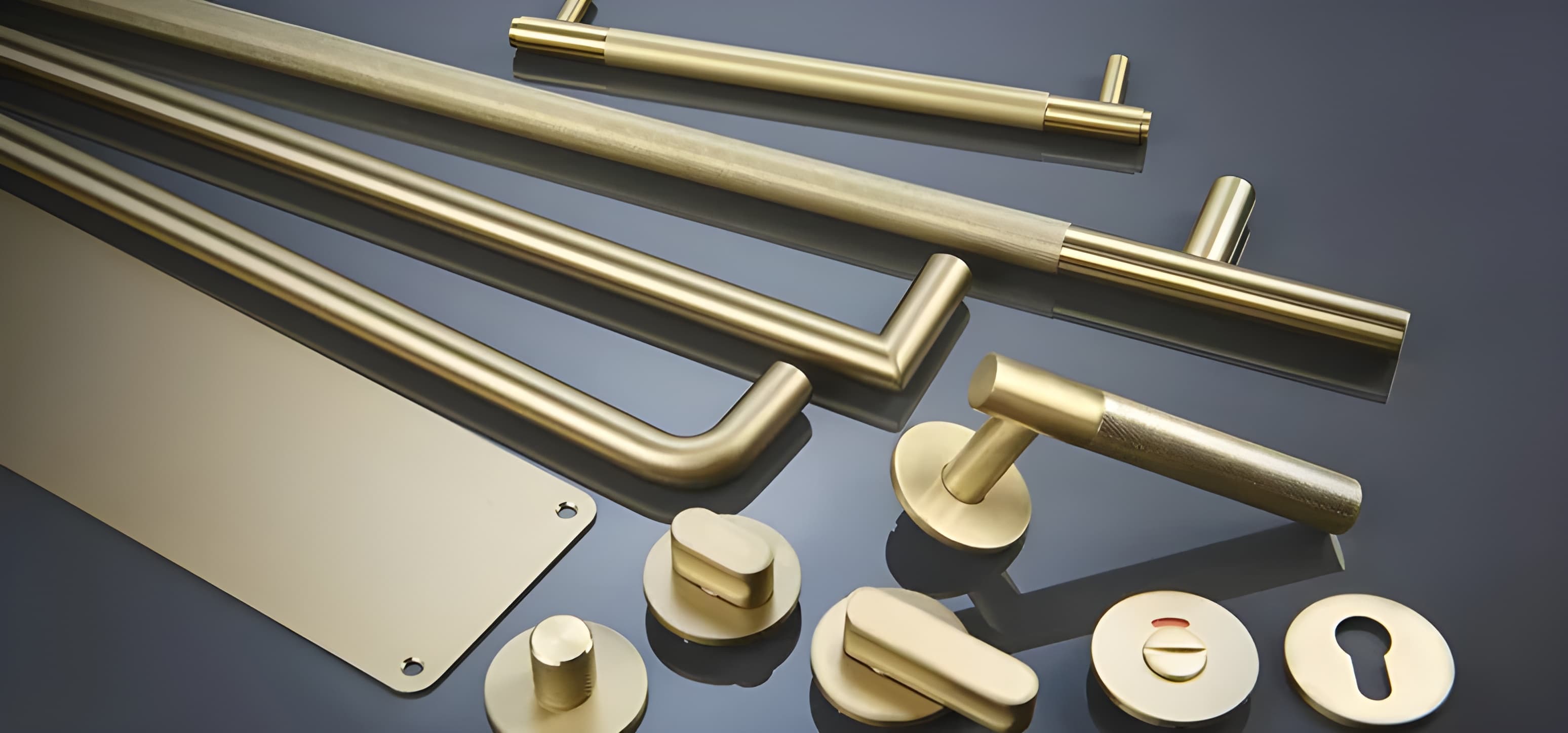 Brass door handles, pull bars and escutcheons laid out on a dark surface